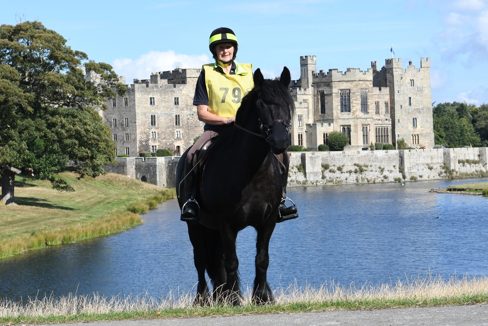 Black mare with rider in high vis vest, in front of Raby castle and moat